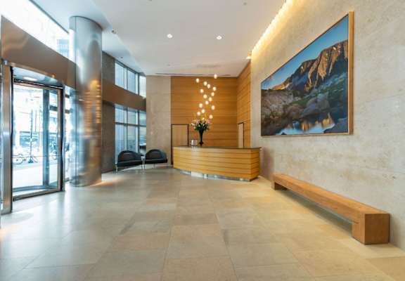 A large painting of a mountain landscape hangs on a wall above a wooden bench in a spacious lobby.