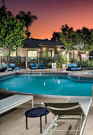 A small pool surrounded by chairs and trees.