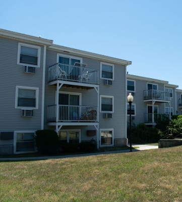 a row of grey apartment buildings with balconies and a grassy area in front of them