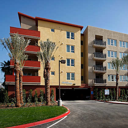 A large apartment complex with a red roof and palm trees in front.