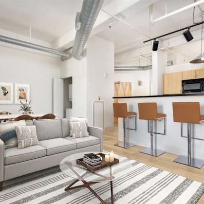 A living room with a grey couch, a coffee table, and a bar area with stools.