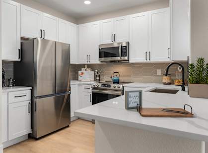 A kitchen with a stainless steel refrigerator, white cabinets, and a white countertop.
