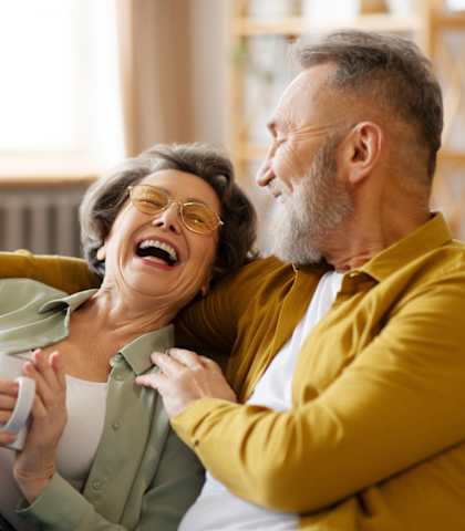 An older couple is sitting on a couch, laughing together.