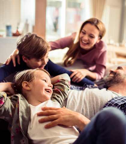 A family of four is sitting on a couch together.