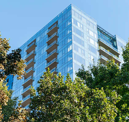 A tall glass building is surrounded by trees.