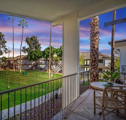 A patio with a table and chairs overlooks a green lawn and trees.