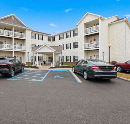 A parking lot in front of a white apartment building with cars parked.