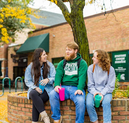 three students sitting on a wall under a tree