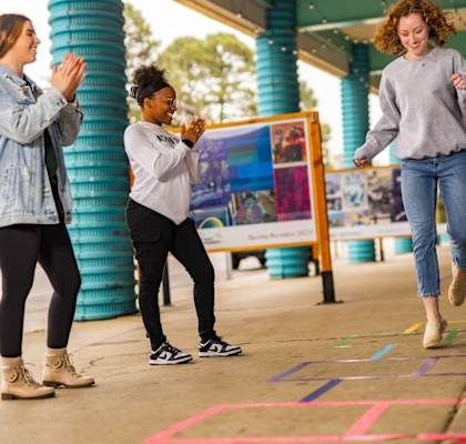 three young women playing hopscotch on a sidewalk