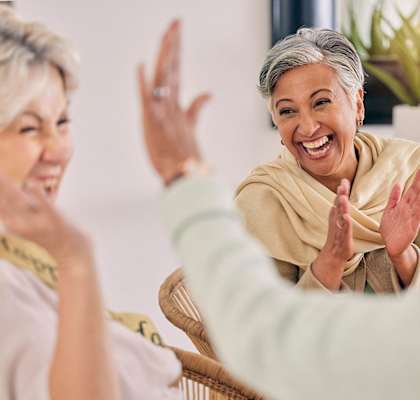 Three women are laughing and clapping their hands together.