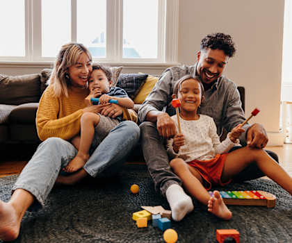 A family of four is sitting on the floor playing with toys.