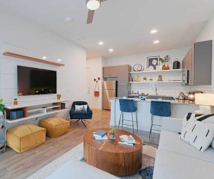 A modern living room with a flat screen TV, a kitchen area, and a coffee table.