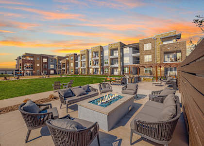 A sunset view of a patio with chairs and a fire pit in front of apartment buildings at Magnolia Grove Apartments, Terrell, 75160