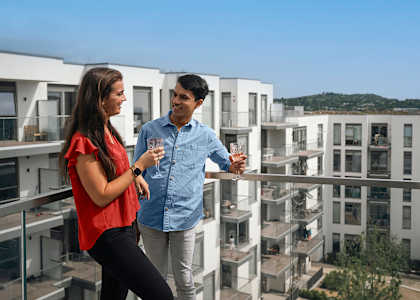 Two people standing on a balcony with apartment buildings in the background.