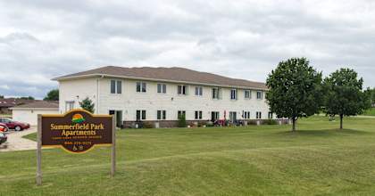 A sign for Summerfield Park Apartments stands in front of a white building.
