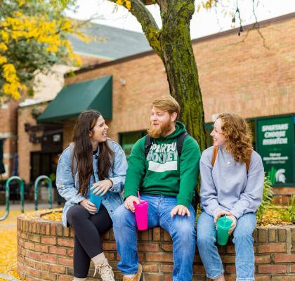 three students sitting on a wall under a tree