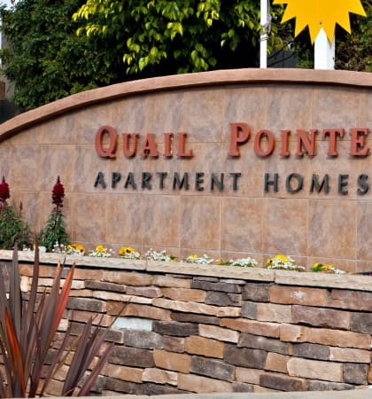 a stone wall with a sign that reads quail pointe apartment homes