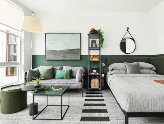 A bedroom with a bed, a couch, a table, and a plant.
