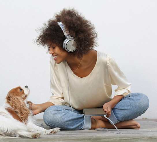 A woman with headphones sitting on the ground petting a dog.