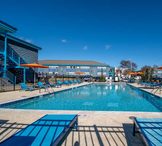 A large outdoor swimming pool with blue loungers and a clear blue sky.