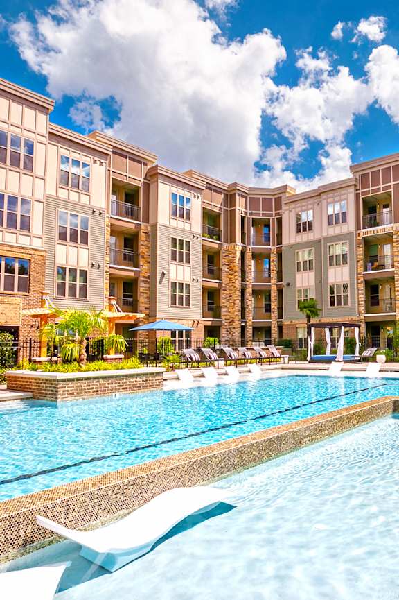 a swimming pool with lounge chairs and umbrellas in front of an apartment building
