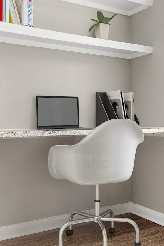 A white chair is in front of a desk with a laptop and a plant on it.