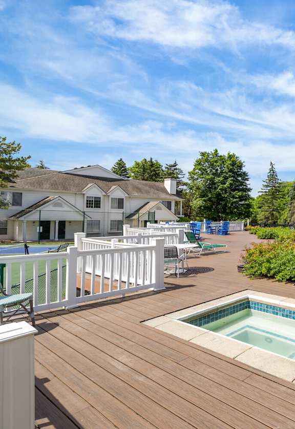 A wooden deck with a hot tub and a pool in the background.