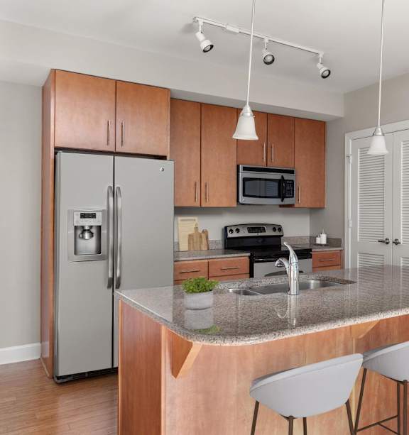 A kitchen with a refrigerator, microwave, oven, sink, and bar stools.