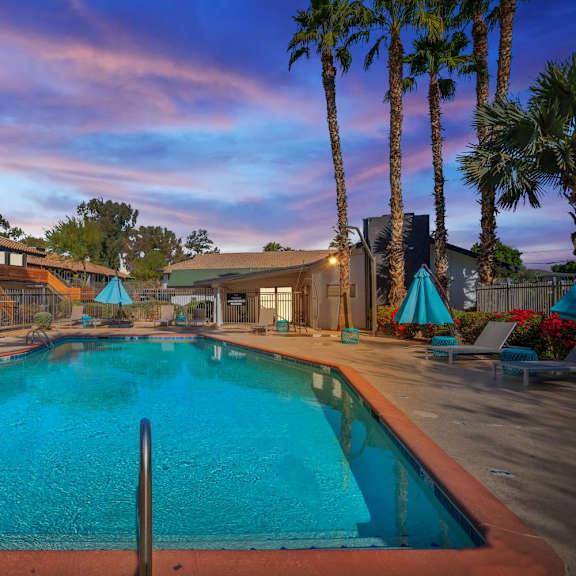 A swimming pool surrounded by palm trees and a sunset sky.