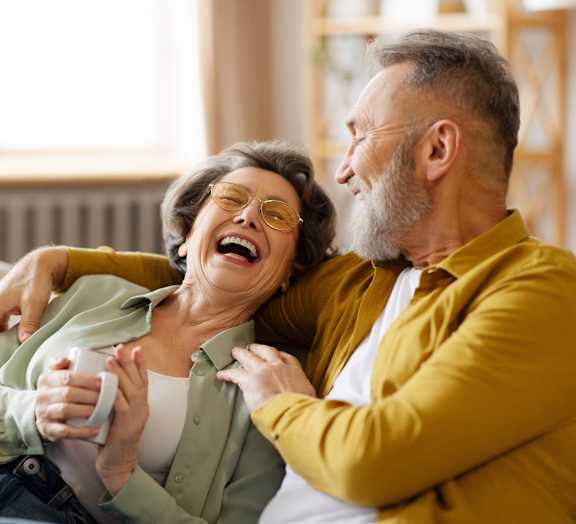 An older couple is sitting on a couch, laughing together.