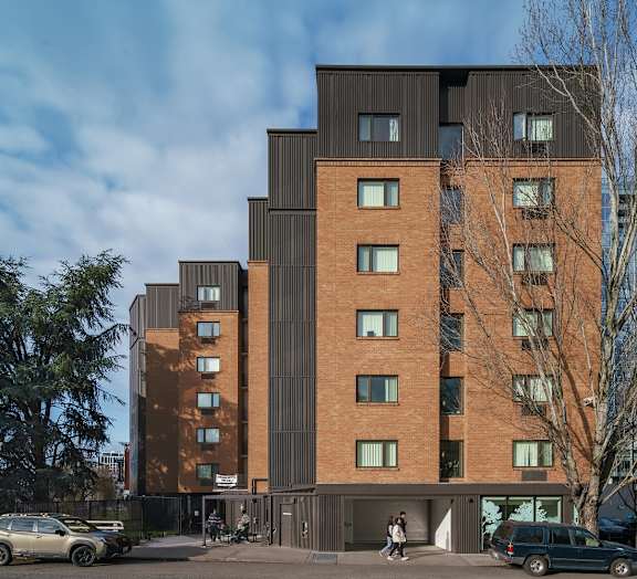 a tall brick building with a black facade and people walking in front of it