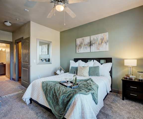 A spacious bedroom with a green accent wall, a queen-size bed with a white and green bedspread, a dresser, wall art, decorations, closet, and nightstands at the Edge at Midtown Apartment Homes. 