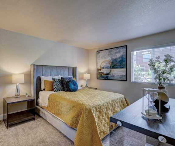 A bedroom with a queen-size bed, a dresser, decorations, closet, and nightstands at Indigo Apartments. 