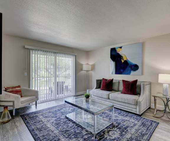 The living room with a couch, plush chairs, coffee table, decorations, a TV, and balcony at Indigo Apartments. 