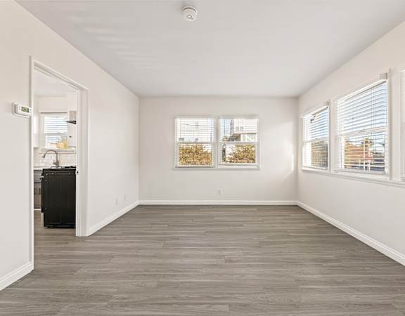 A room with a wooden floor and two windows with blinds.