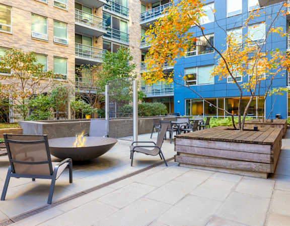 an outdoor patio with chairs and a fire pit in front of an apartment building