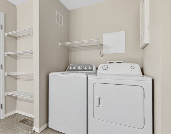an empty laundry room with a washer and dryer and a closet with shelves