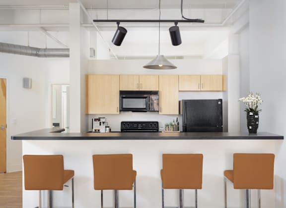 A kitchen with a black countertop and brown chairs.