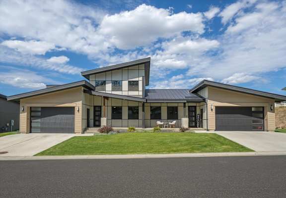 A modern house with a large front yard and two garages.