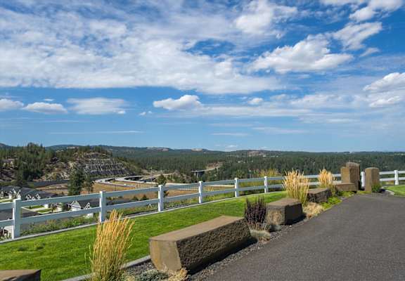 A white fence runs along a grassy area with a road leading to a white house.