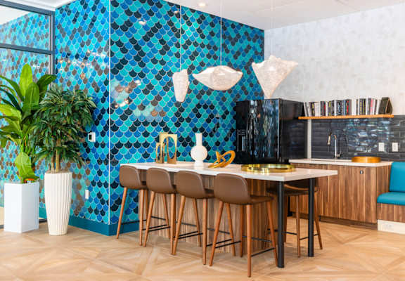 A kitchen with a blue tiled wall and wooden chairs.