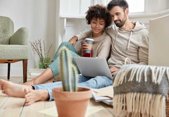 a man and woman sitting on the floor with a laptop