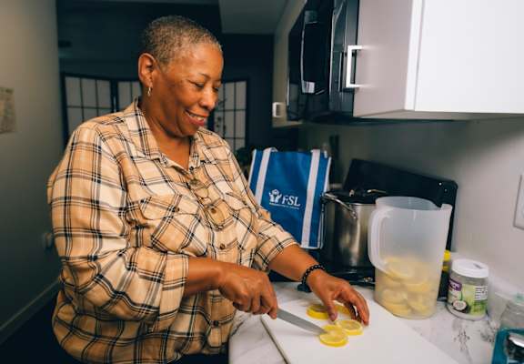 A woman in a plaid shirt is cutting up yellow food on a white counter.