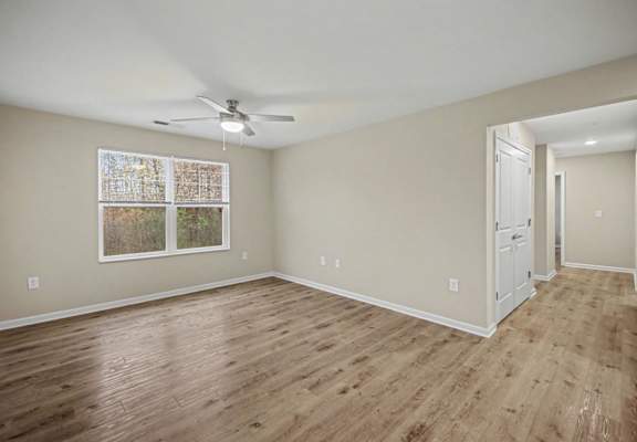 A room with a ceiling fan and a window with a picture hanging on the wall.