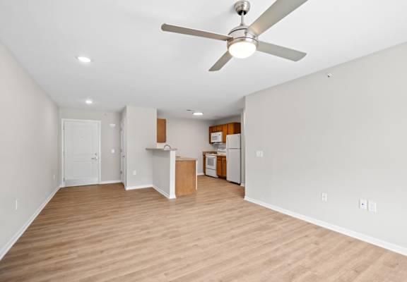 an empty living room with a ceiling fan and a kitchen