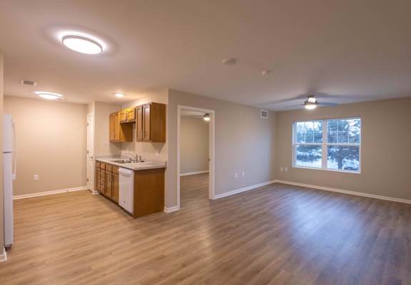 A kitchen with wooden floors and a refrigerator on the left.