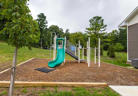 A playground with a green slide and a brown surface.