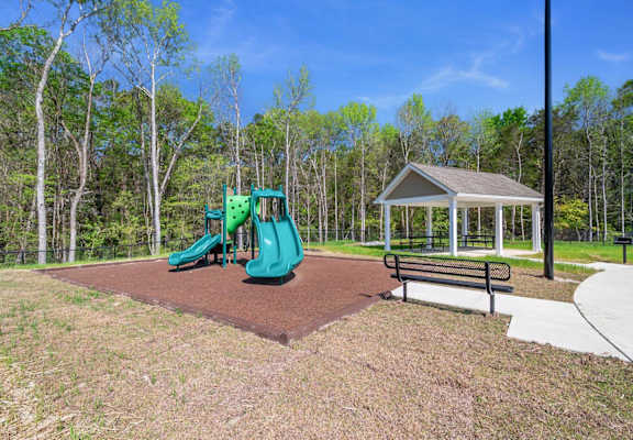 A playground with a green slide and a bench next to a gazebo.