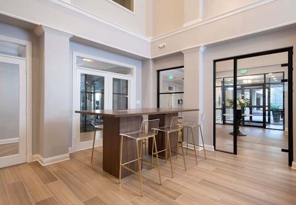 A modern bar area with a wooden counter and stools. at Vivant Woodholme, Pikesville
