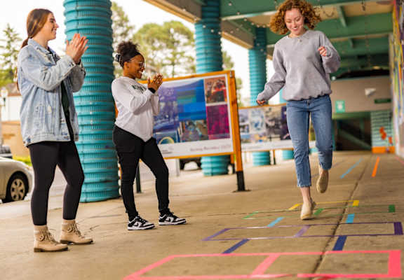 three young women playing hopscotch on a sidewalk